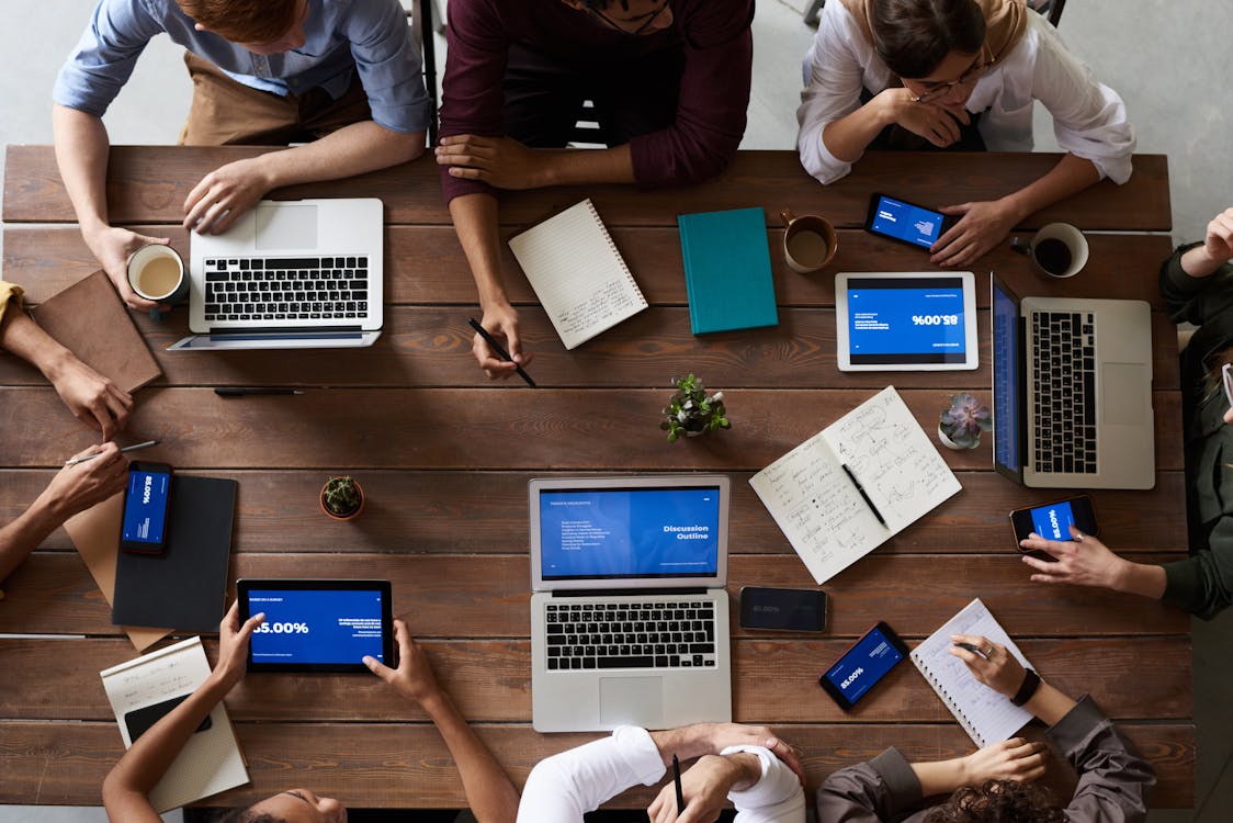 a group of people sitting around a table with laptops and tablets